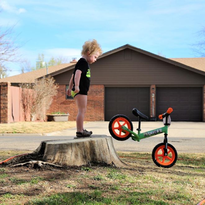 Boy stands in his underwear and rolls 12" Strider Sport off a stump