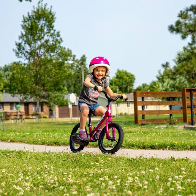 A girl confidently pedals on her fuchsia pink Strider 14x Sport